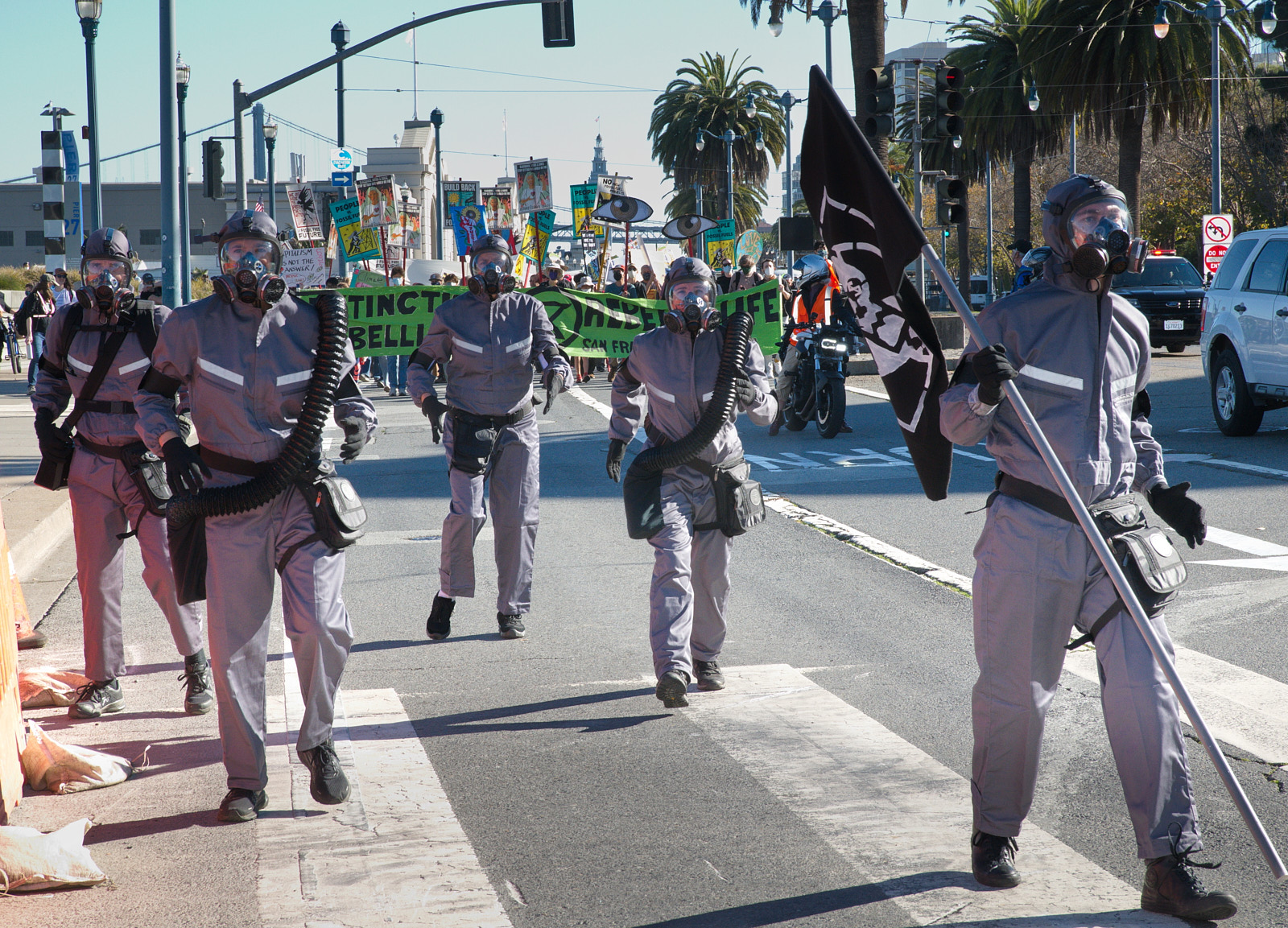 Street Theater Five characters walk down the street in San Francisco, wearing masks and grey hazmat suits