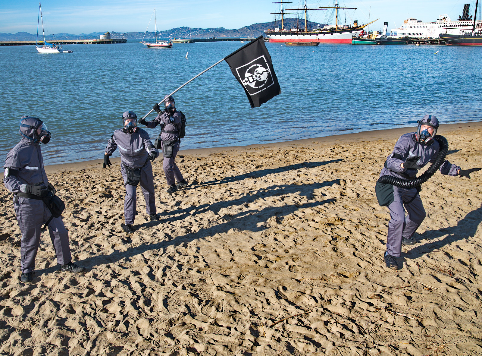 Xtractors Xtractors dressed in grey hazmat suits stand on a beach with a black flag