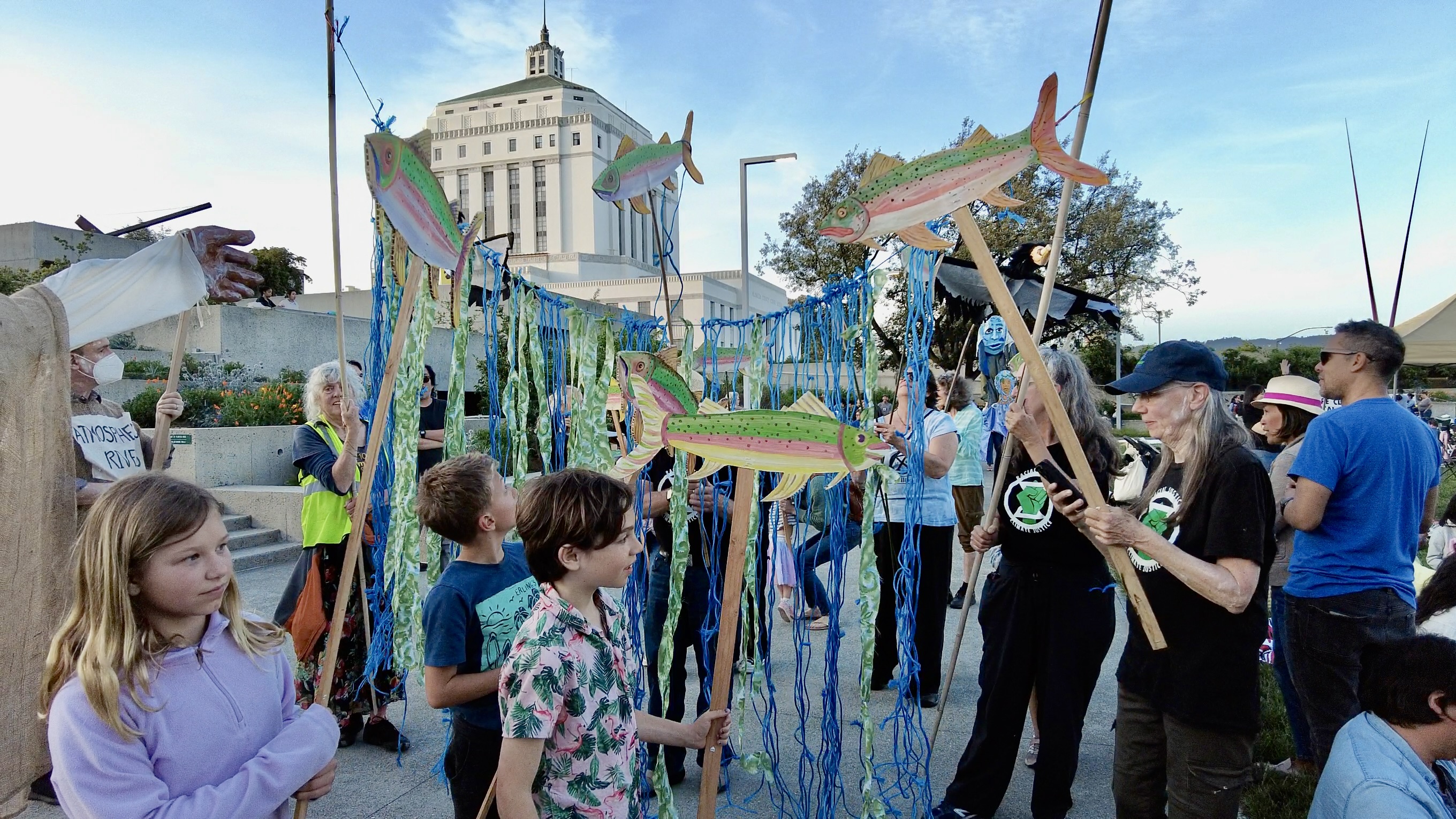 Kelp Forest Youth and adults stand in a plaza holding blue and green banners and painted salmon